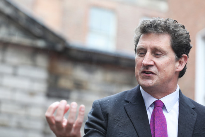 Minister for Transport Eamon Ryan - wearing a dark suit jacket, light shirt and pink tie - talking and making hand gestures alongside his speech.