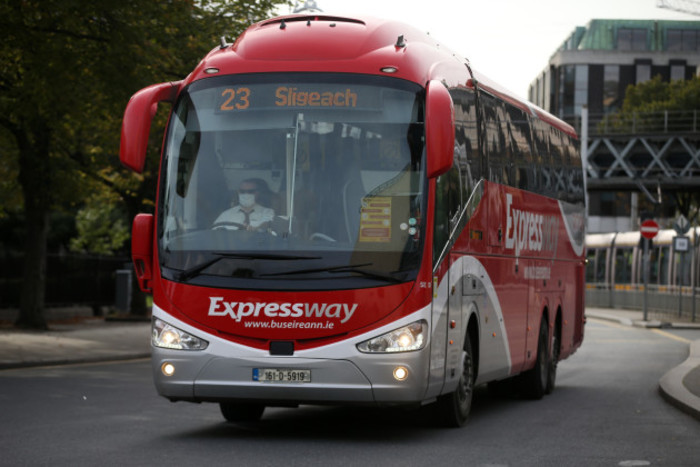 A single decker red coach with Expressway and Sligo written on the front. It is near Bus&aacute;ras as the Life Centre on Abbey Street is visible. A Luas and some trees are also visible in the background.