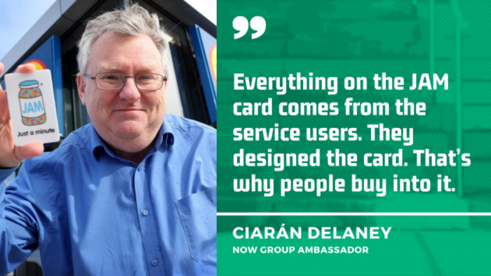 Ciar&aacute;n Delaney, NOW Group Ambassador, wearing a blue shirt and holding a JAM card which has a drawing of a pot of jam and the writing &lsquo;Just a minute&rsquo; on it, with the quote - Everything on the JAM card comes from the service users. They designed the card. That&rsquo;s why people buy into it.