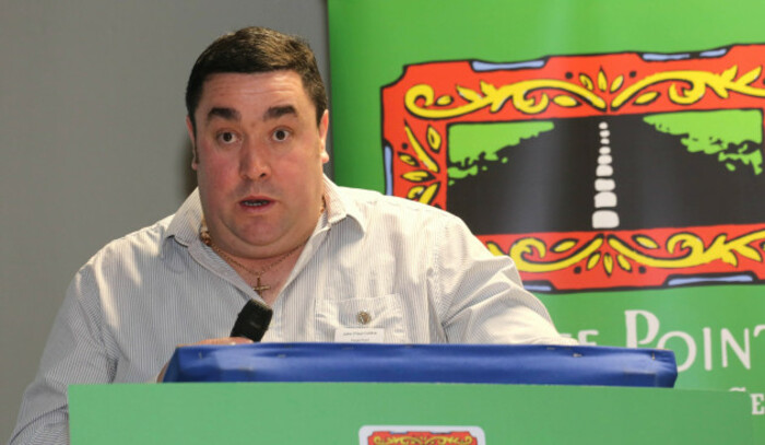 John Paul Collins - wearing a white shirt - standing at a podium at an event