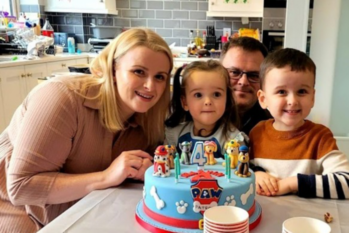 The Moore family - Kim and Simon and their daughter Megan and son Marvin - smiling while at the kitchen table which has a Paw Patrol birthday cake on it.