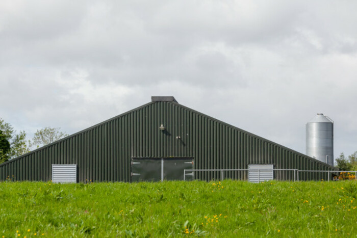 The front of a green poultry shed with a grain silo in the background