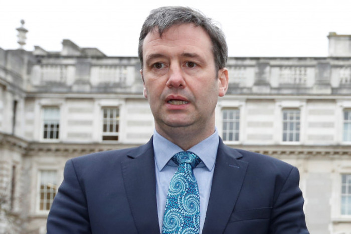 Michael D'Arcy standing outside wearing a light blue shirt, blue patterned tied and grey suit jacket.