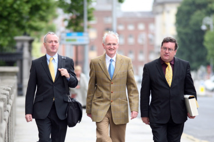 D&oacute;nal Geoghegan walking down a Dublin Street wearing a suit and shoulder bag. Walking beside him are then-Green Party chairman John Gormley wearing a tan suit, and talks negotiator Dan Boyle wearing a yellow tie and black suit. 