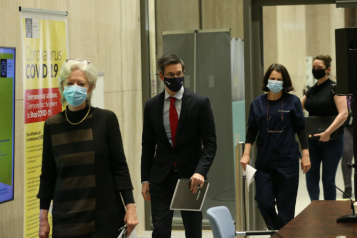 Four masked experts walking into a HSE briefing with a Covid-19 sign in the background