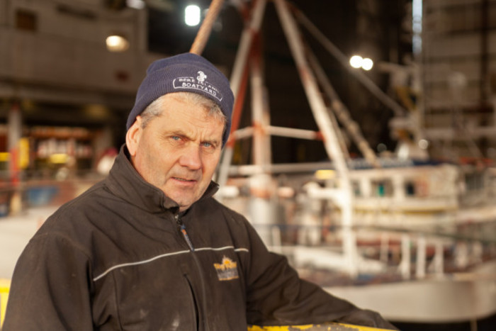 Gerard Sullivan in a dark jacket and hat standing in front of a boat yard