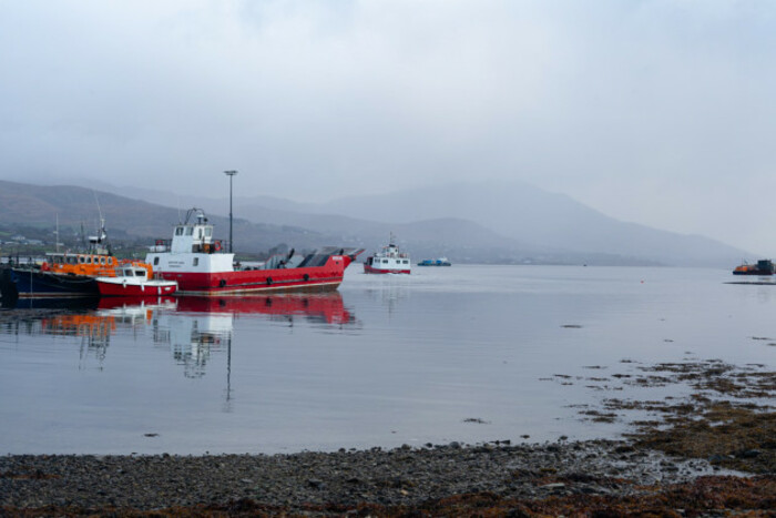 Several boats tied up at the pier on Bere Island with the mainland in the background