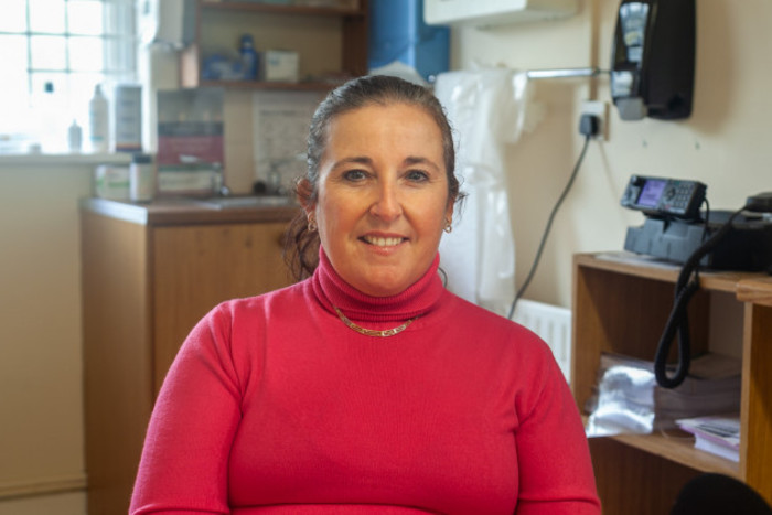 Dr Noreen Lineen-Curtis smiling in a red jumper in her health clinic