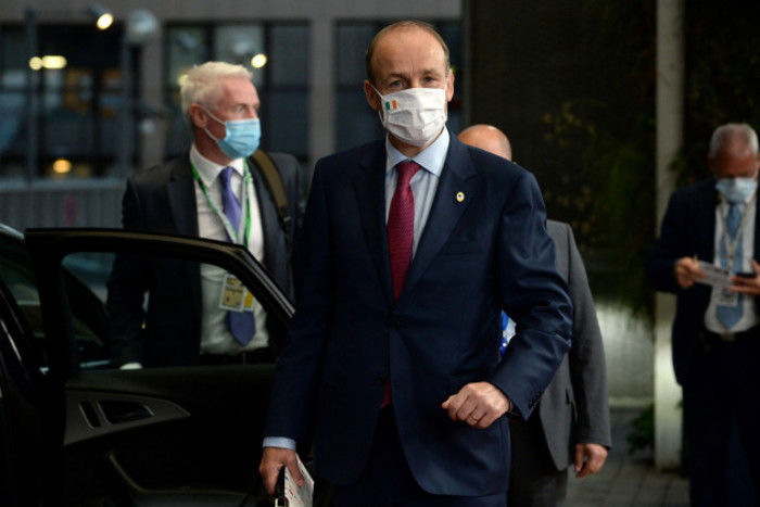 Miche&aacute;l Martin wearing a suit and face mask standing beside the open door of a car. 