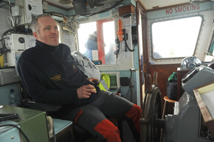 Skipper Alan O'Grady in a blue pullover sitting in captain's seat of his boat. 