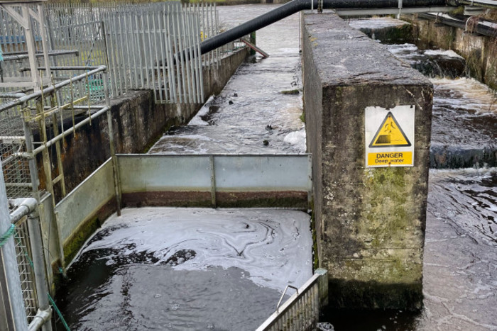 Fish pass made up of concrete and metal structures with steps down with water running over them. A sign says: Danger - Deep Water. 