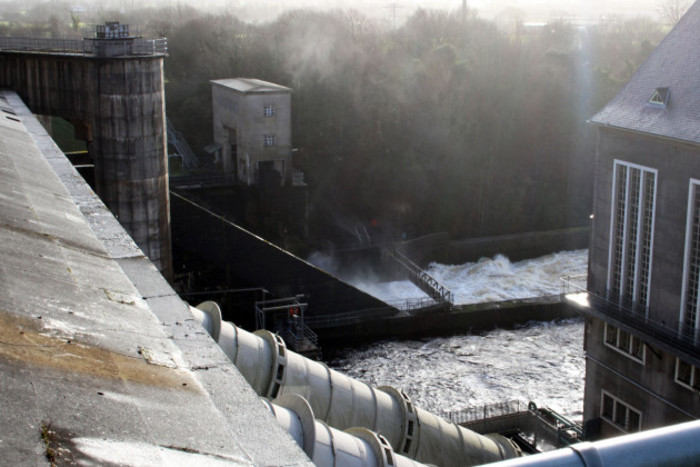 View from the top of the dam at Ardnacrusha with large pipes coming down from it in the foreground and turbulent water seen at the bottom. 