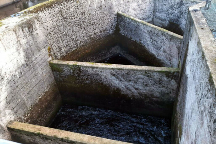 A channel made of concrete with walls of varying heights, also made of concrete, with water inside, with a gap between the top of the walls and the water.