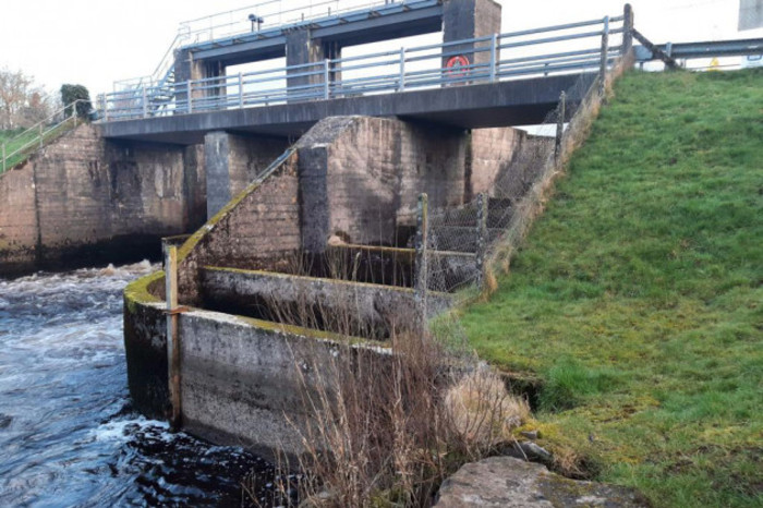 Weir on a river made of concrete with concrete steps in the foreground with gaps in between. 