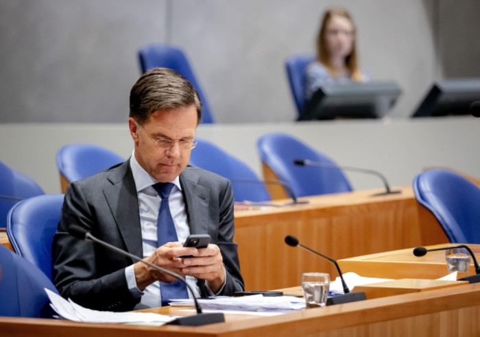 Rutte - wearing a grey shirt and blue tie - sitting in the Dutch Parliament looking at his phone.