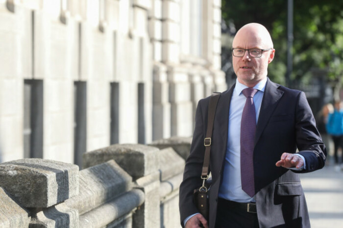 Donnelly walking towards Leinster House carrying a shoulder bag and wearing a dark suit, light shirt and dark tie.