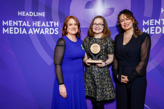 Maria holding the wooden award wearing a black and gold dress, with Nicola and &Aacute;ine on either side.