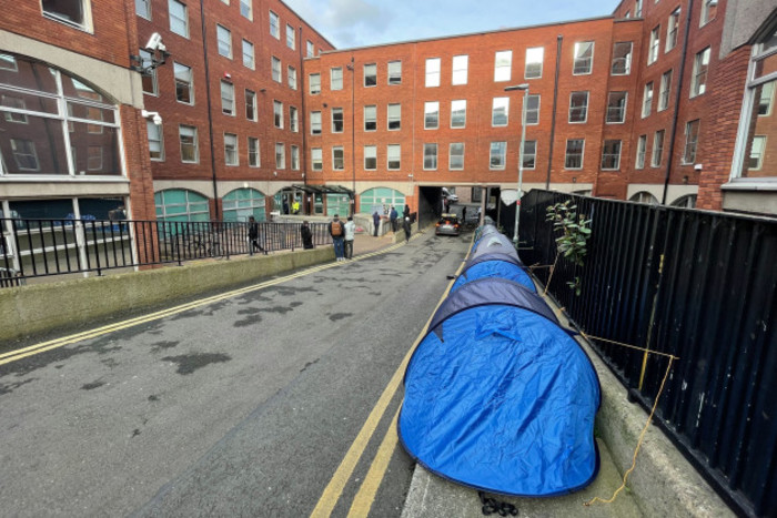 There is a blue tent at the head of a line of tents on the road stretching from the foreground to the back of the photo. To the left is the entrance to the International Protection Office.