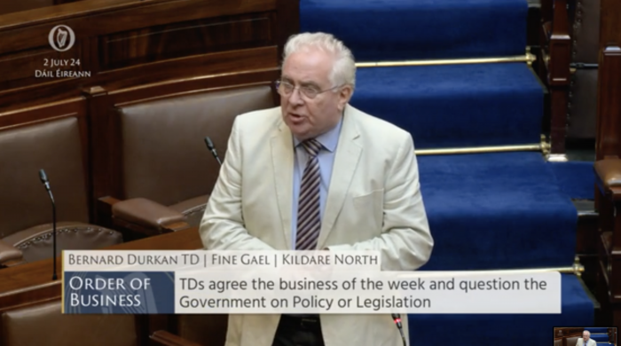 Durkan dressed in a shirt, tie and white jacket speaking in the Dail chamber.